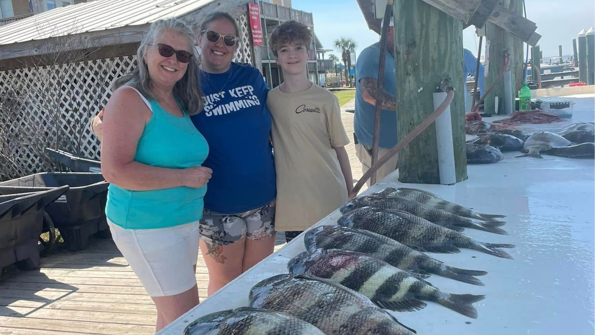 Three people standing beside a docked table of freshly caught fish on a sunny beach dock