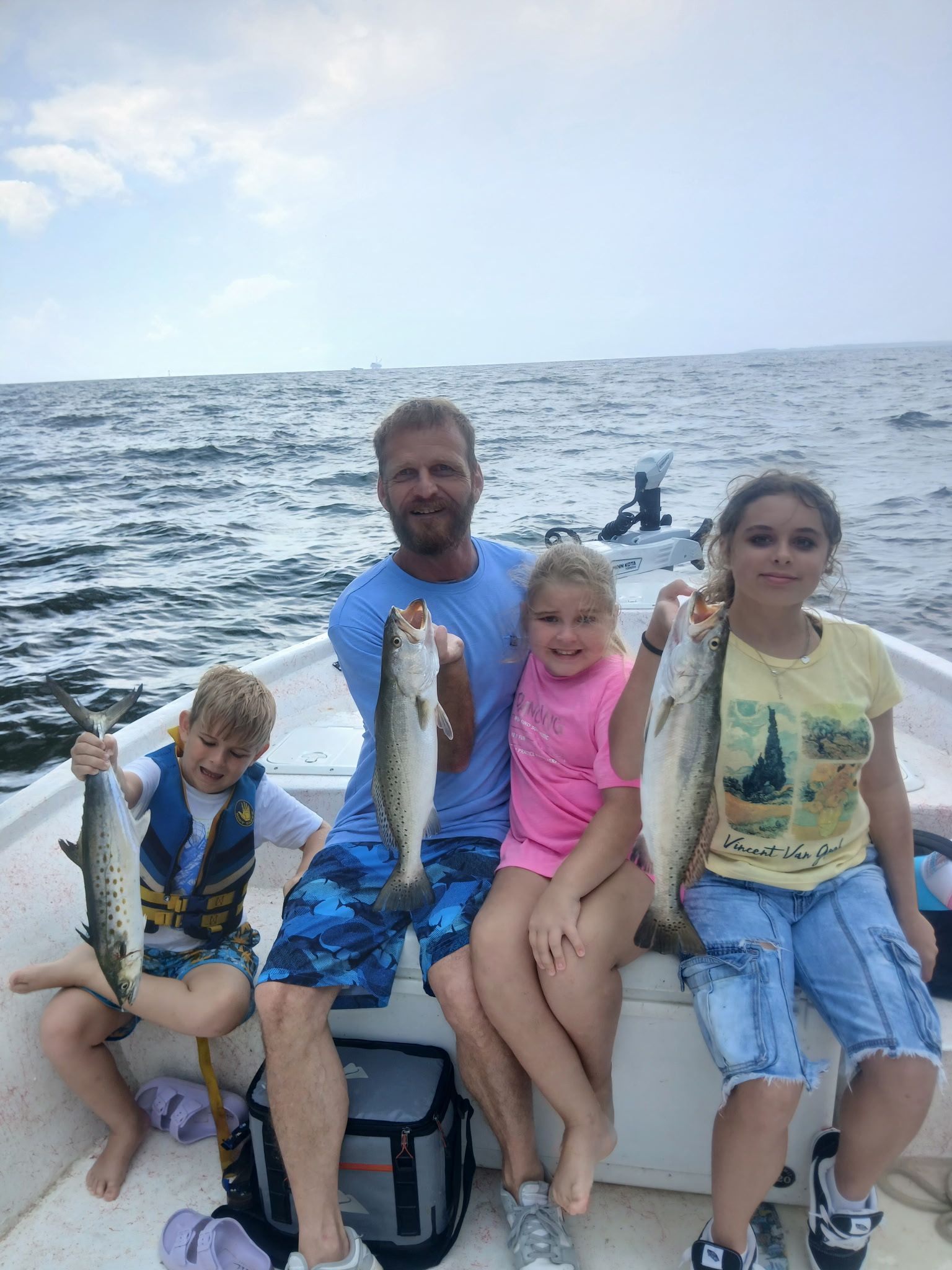 Four people on a boat holding up fish, with ocean and sky in the background.