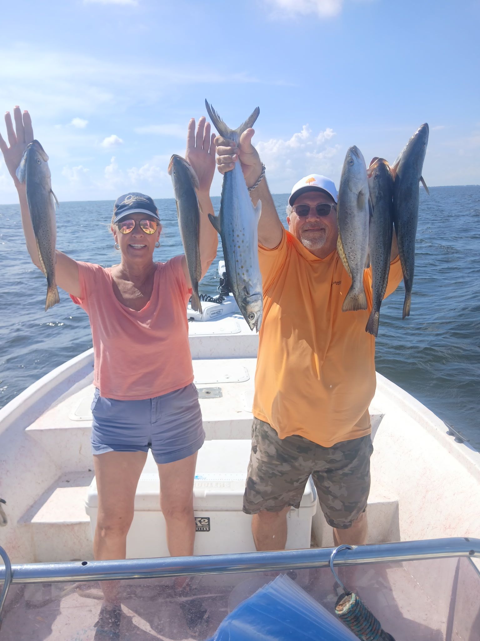 Two people on a boat hold up several fish against a bright blue ocean sky.