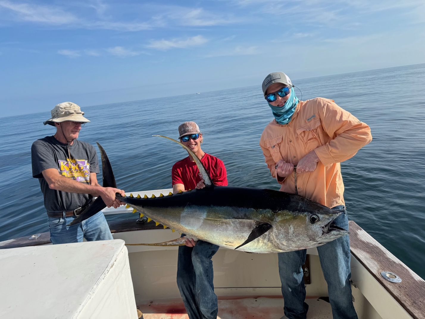 Three anglers on a boat holding a large fish over calm ocean water