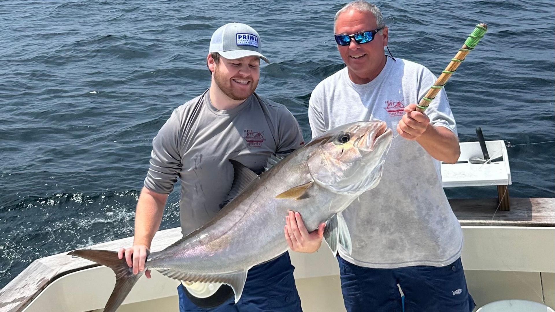 Two men on a boat proudly holding a large silver fish on a sunny day.
