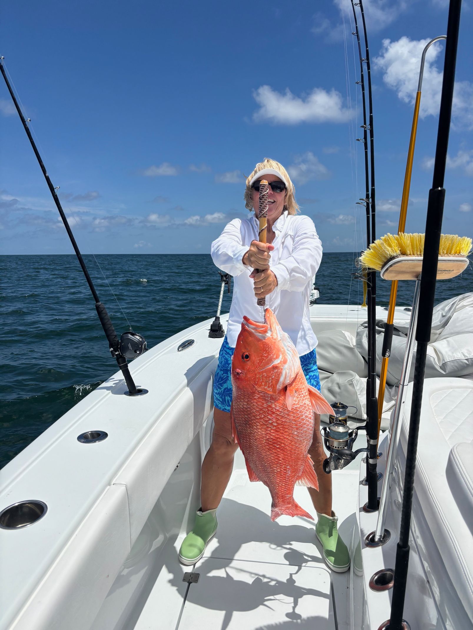 Person on a fishing boat holding a large red fish against a blue ocean and sky.