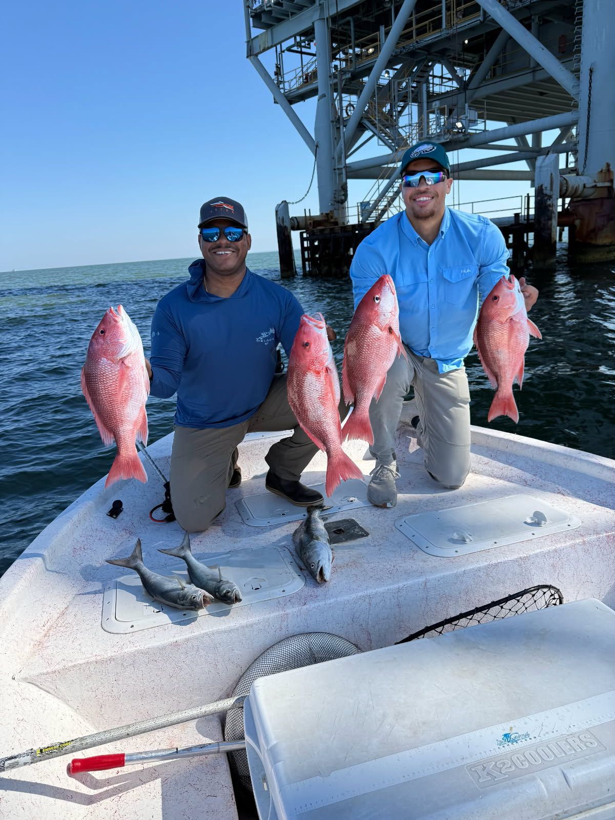 People standing beside a long table of freshly caught red fish at a dock under a wooden shelter