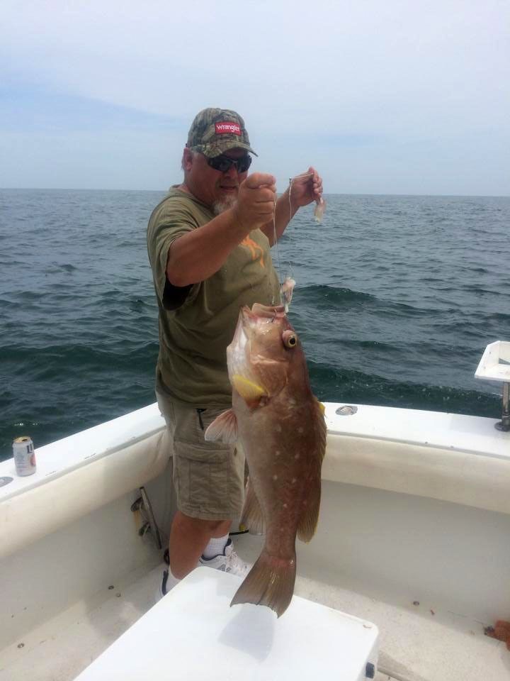A person wearing a camo hat and sunglasses holds a large, brown speckled fish while standing on a boat at sea.