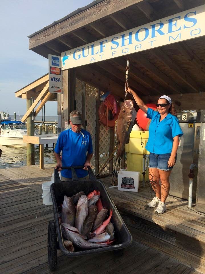 Two people holding a large fish next to a wagon full of fish on a dock at a Gulf Shores marina.