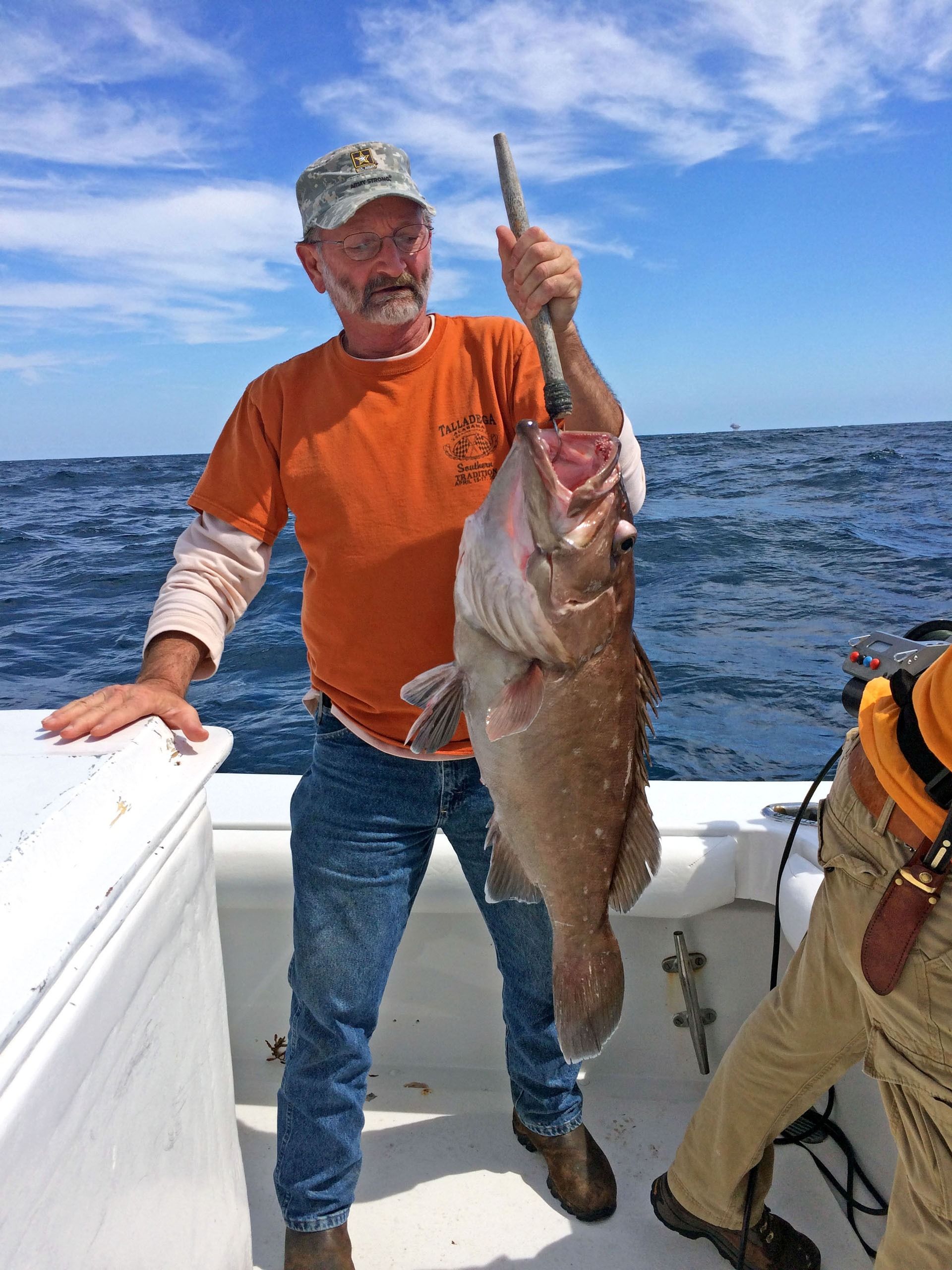A person standing on a boat deck holding a large, caught fish by its mouth using a gaff.