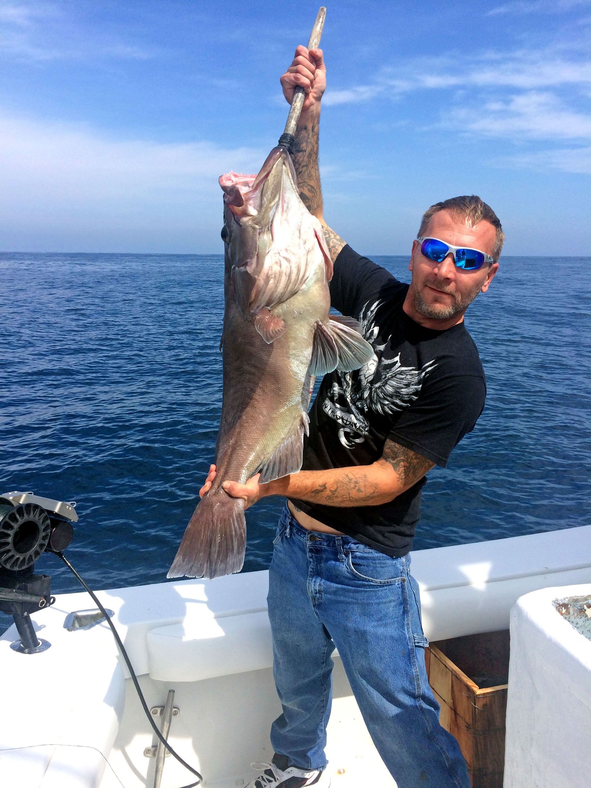 A person holding a large fish by the mouth while standing on a boat on the ocean.