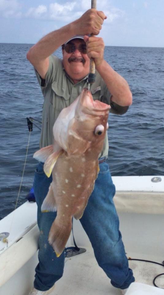 A man on a boat holds up a large spotted fish with bulging eyes.