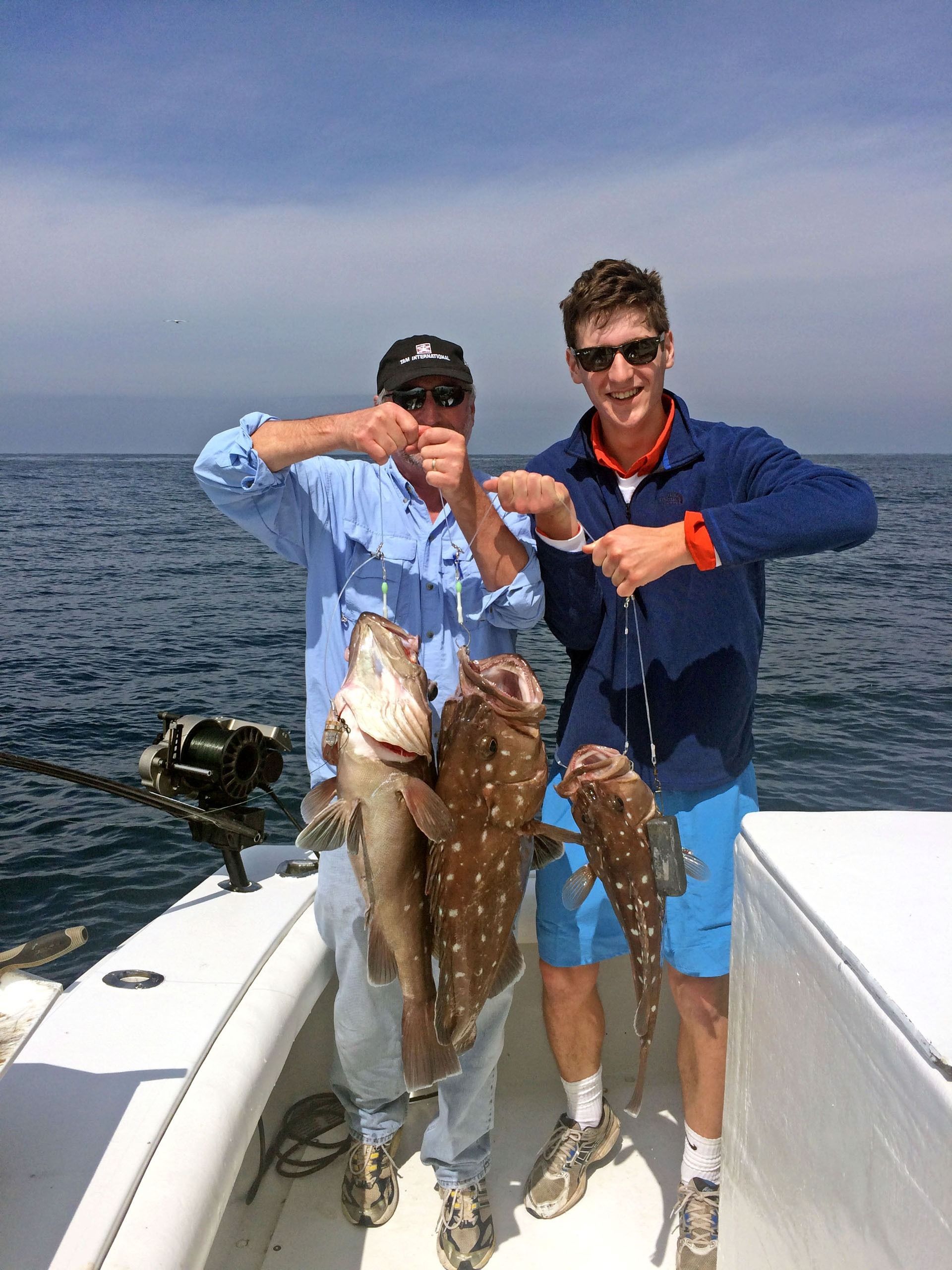 Two people holding up three fish while standing on a boat on the ocean.