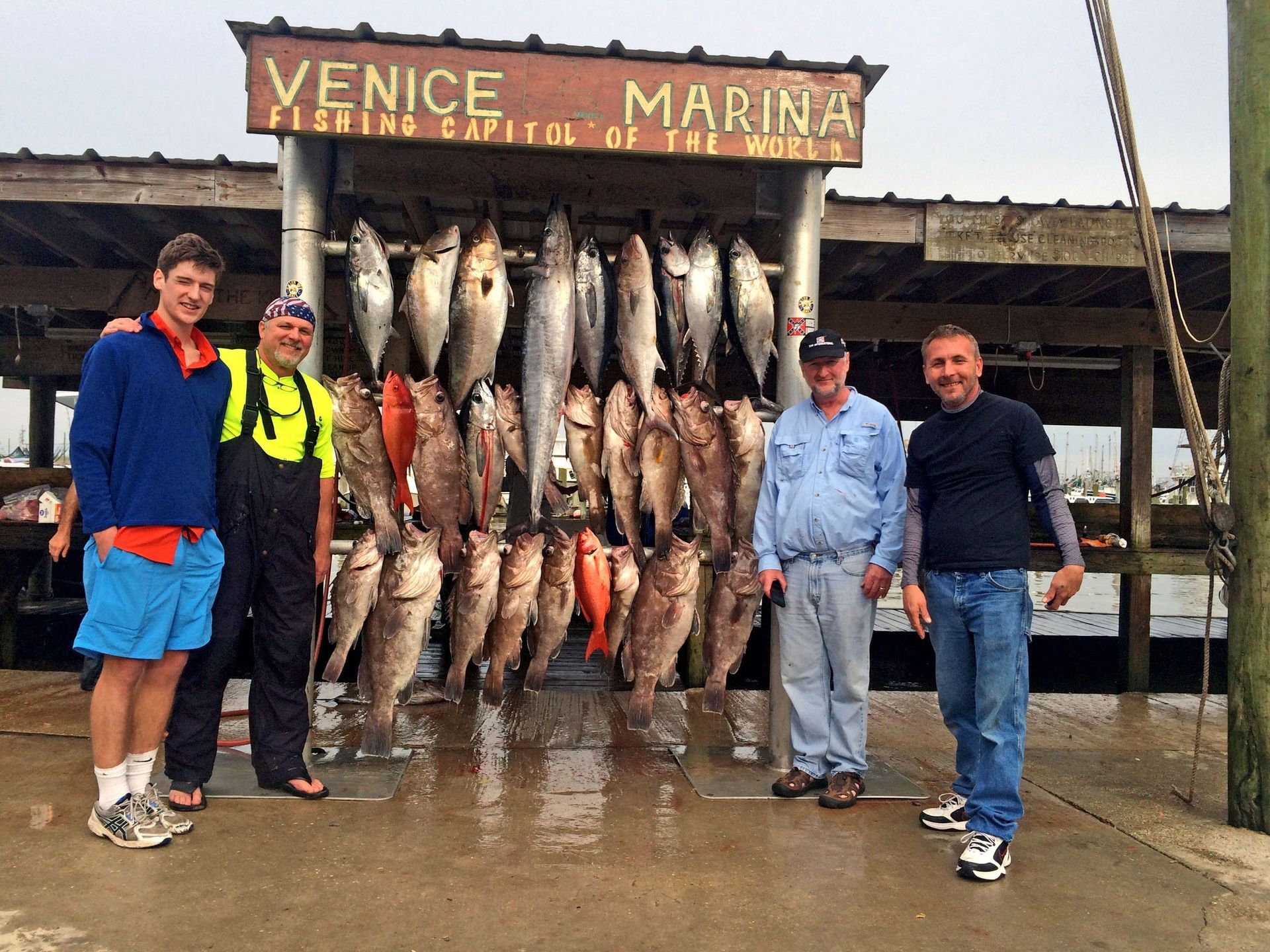 Four people stand under a Venice Marina sign in front of a rack displaying numerous caught fish.