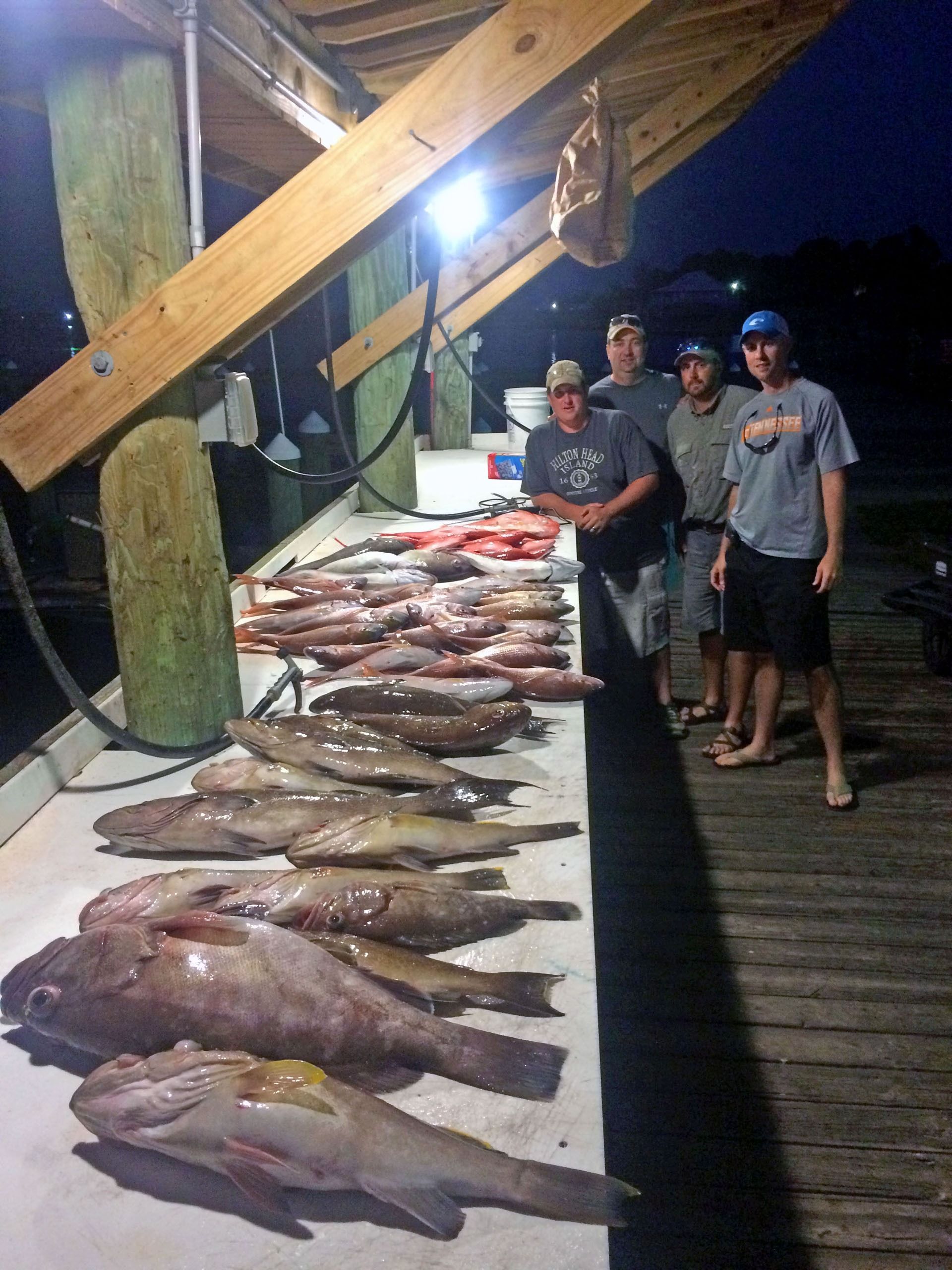 Four people stand by a cleaning station at night with a large catch of fresh fish laid out on the table.