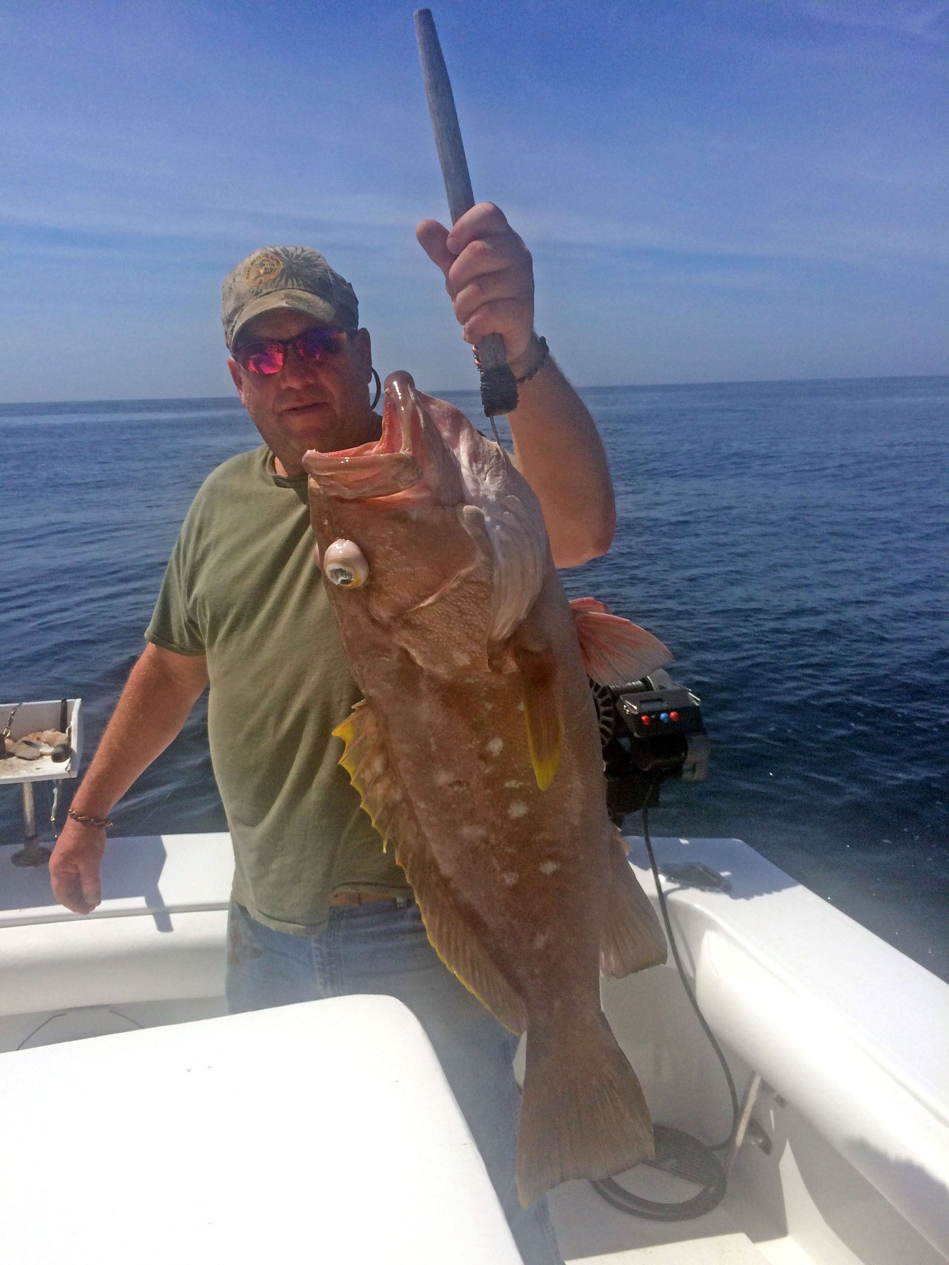 A person holding a large grouper fish while standing on a boat in the ocean.