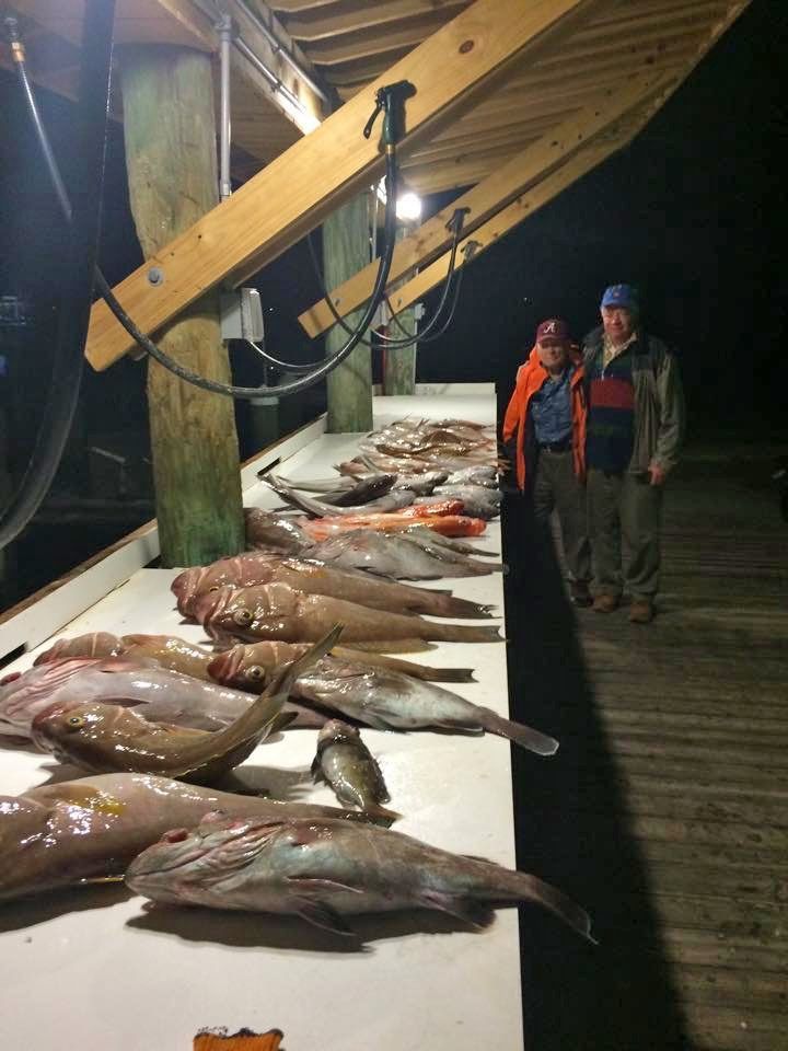 Two people stand by a long outdoor cleaning table covered in numerous freshly caught fish at night.
