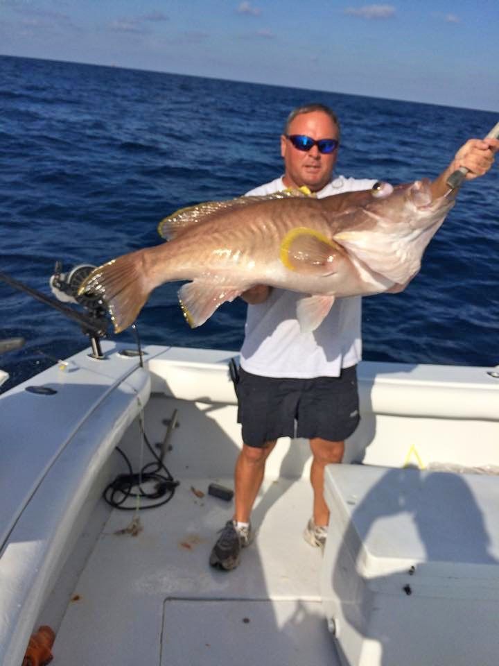 A person stands on a boat deck holding a large, light-brown golden tilefish caught at sea.