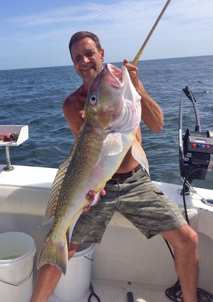 A person on a boat holding a large, golden-hued fish by a fishing line.