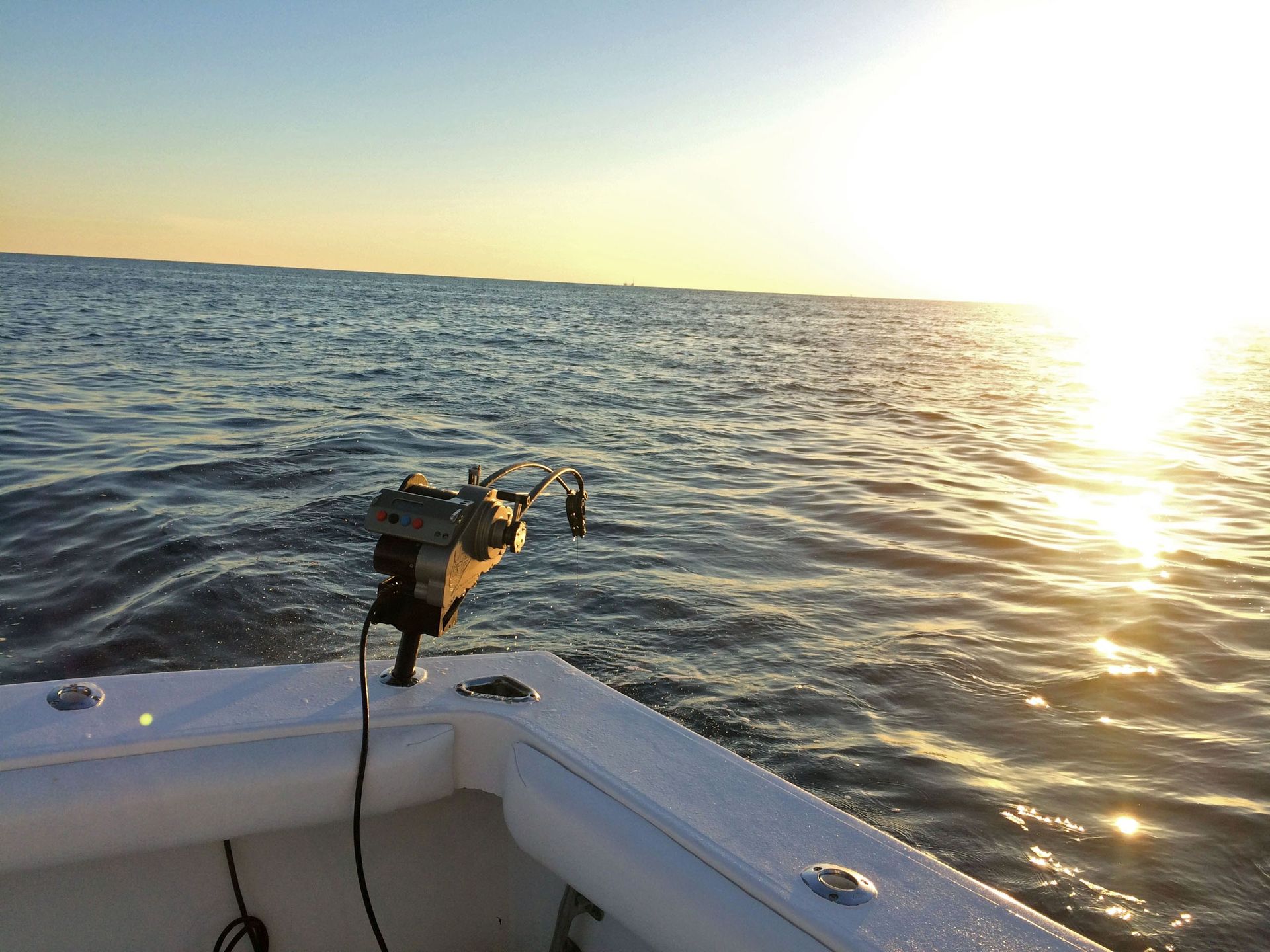 A fishing downrigger mounted on the stern of a boat during a bright, sunny day on the open water.