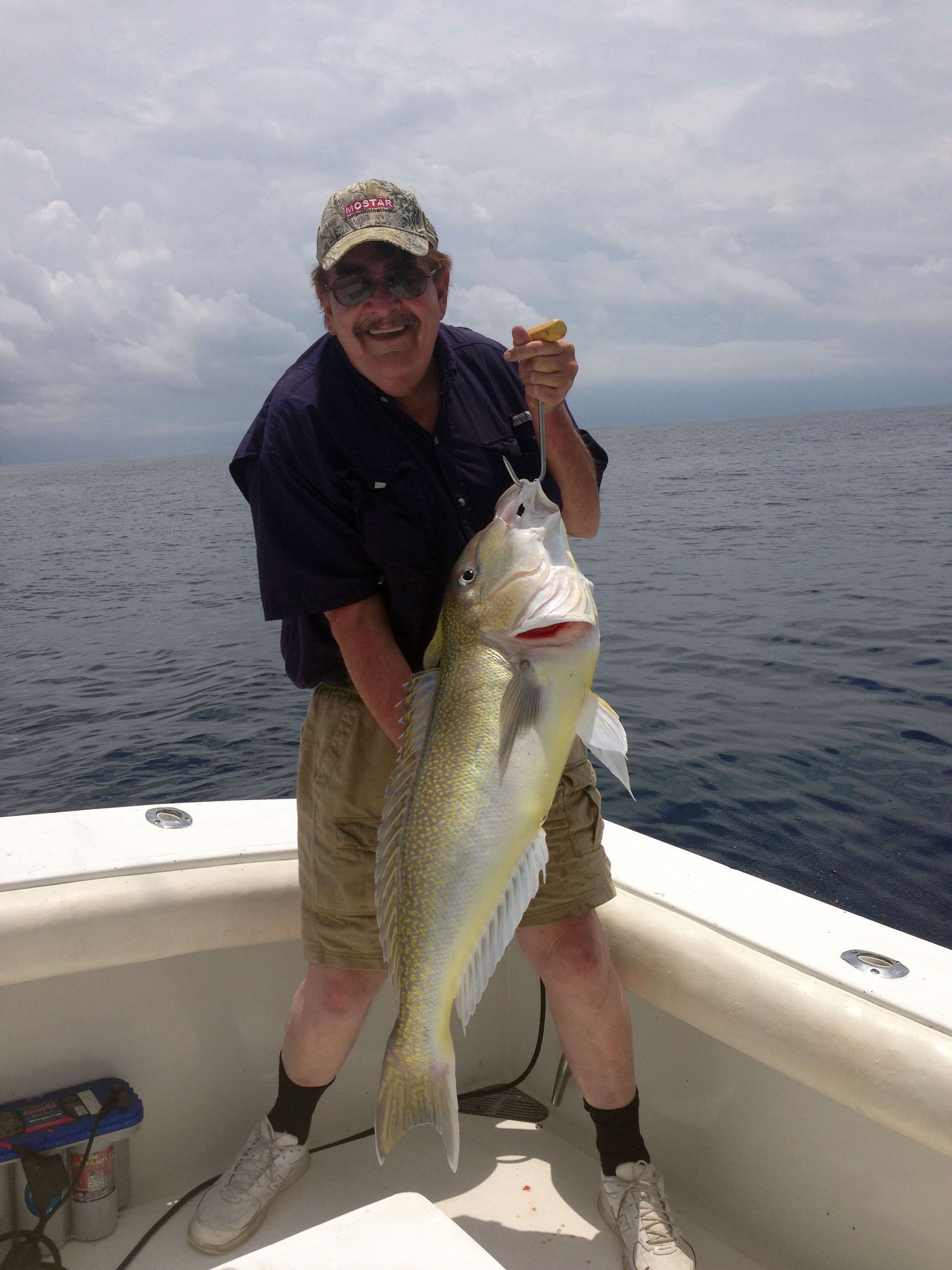 A person on a boat holding up a large caught fish with the ocean in the background.