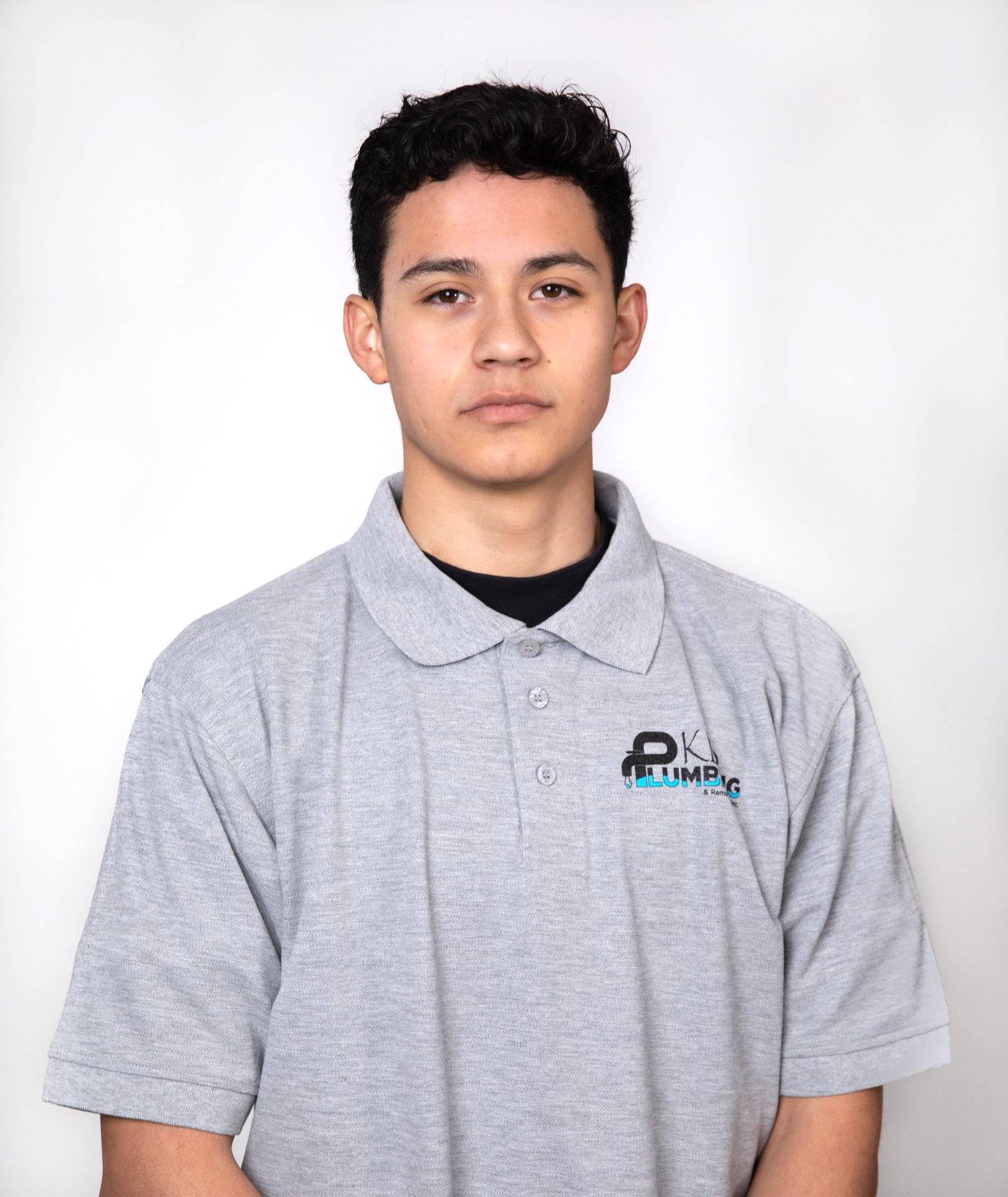 Man in grey polo shirt, looking at camera. The shirt has a logo on the chest.