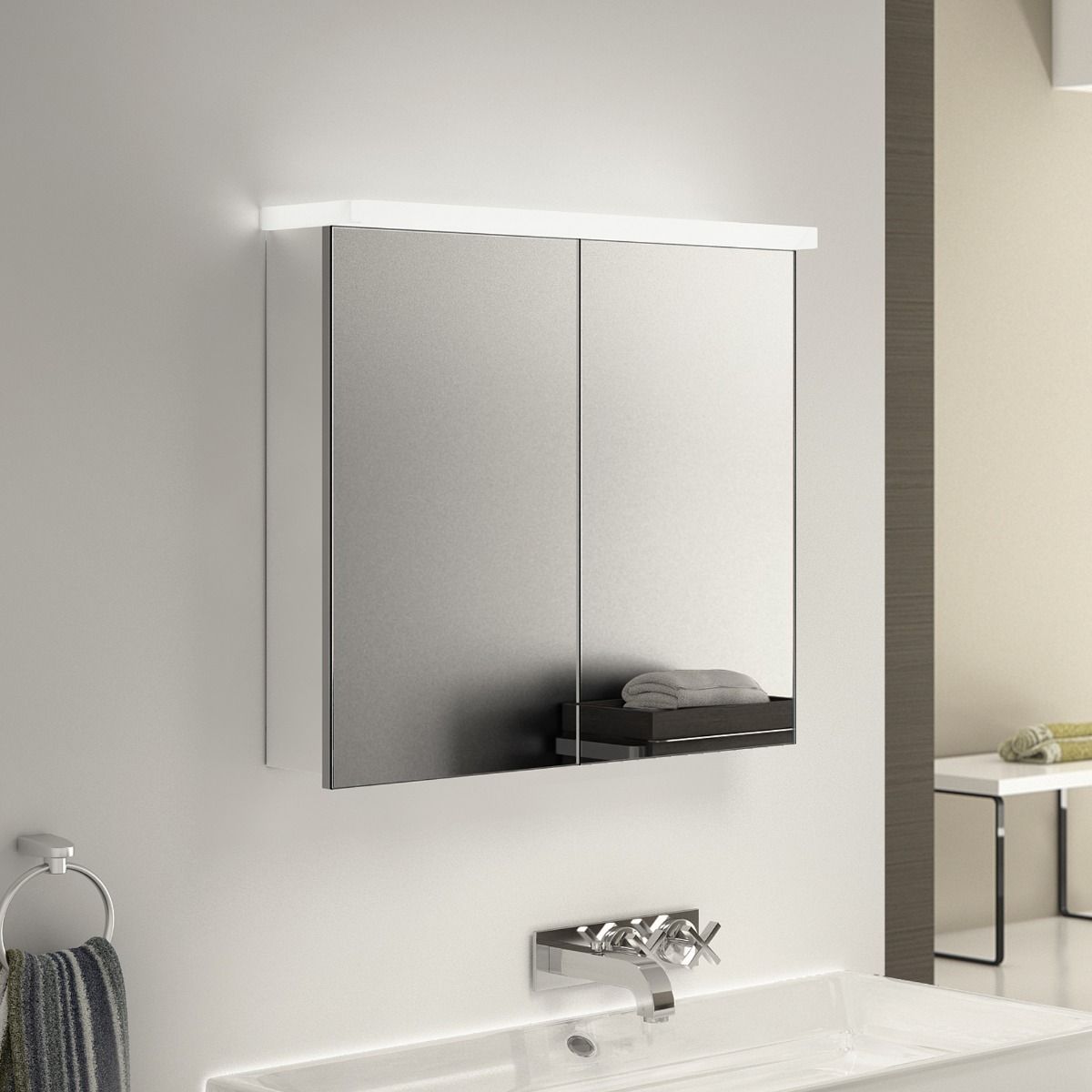 Bathroom medicine cabinet with mirrored doors, illuminated by overhead light; a washbasin is below.