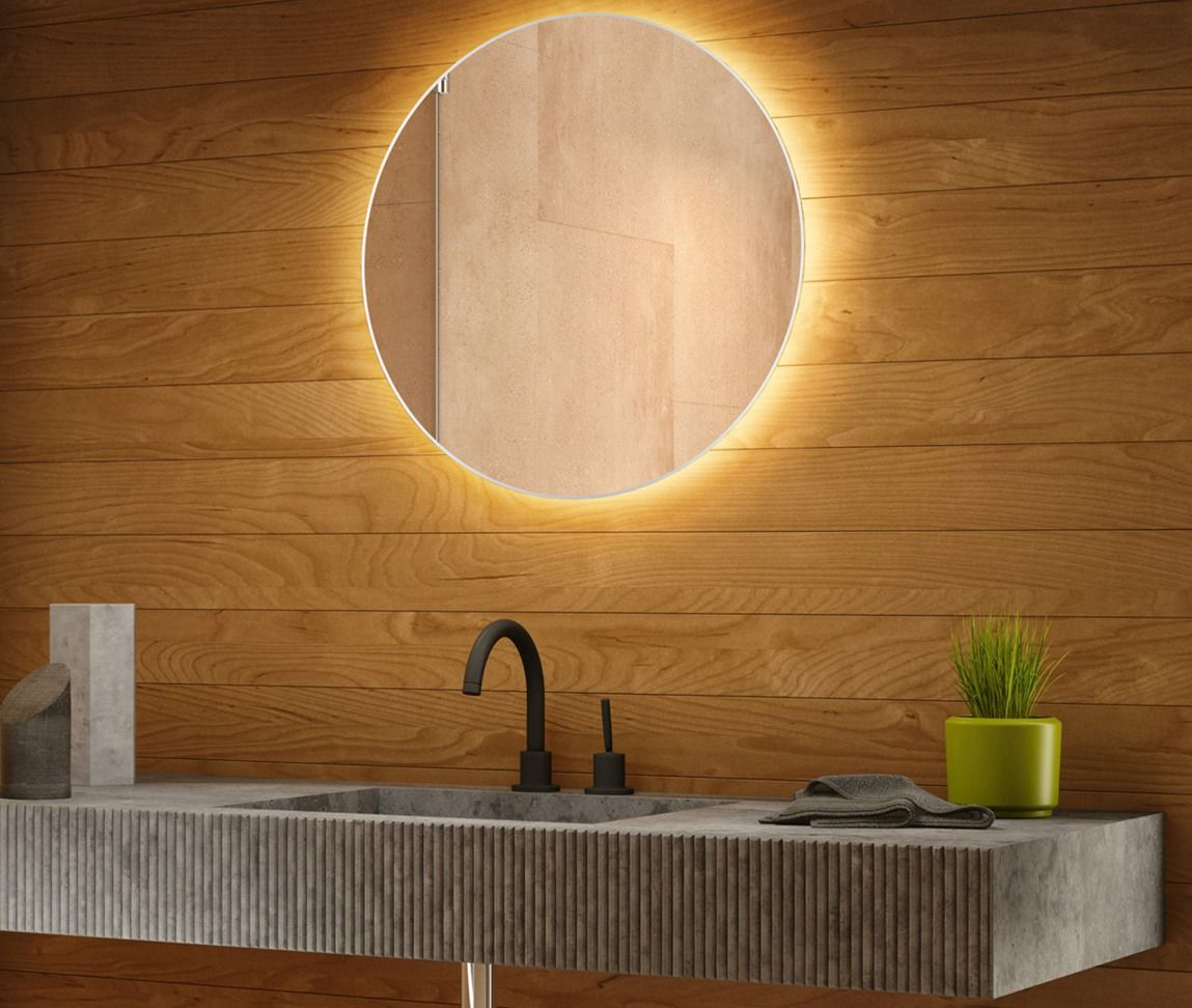 Round lighted mirror over a bathroom sink with wood paneling.
