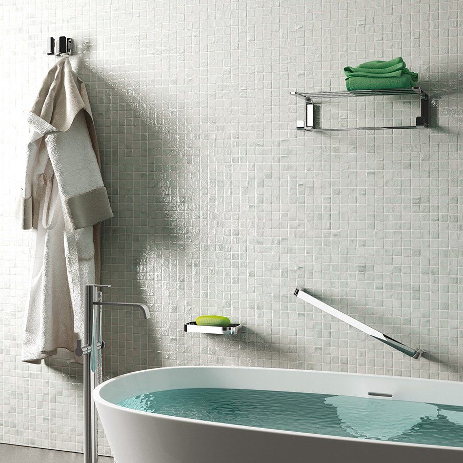 Modern bathroom with a white tub, robe, and chrome fixtures against tiled walls.