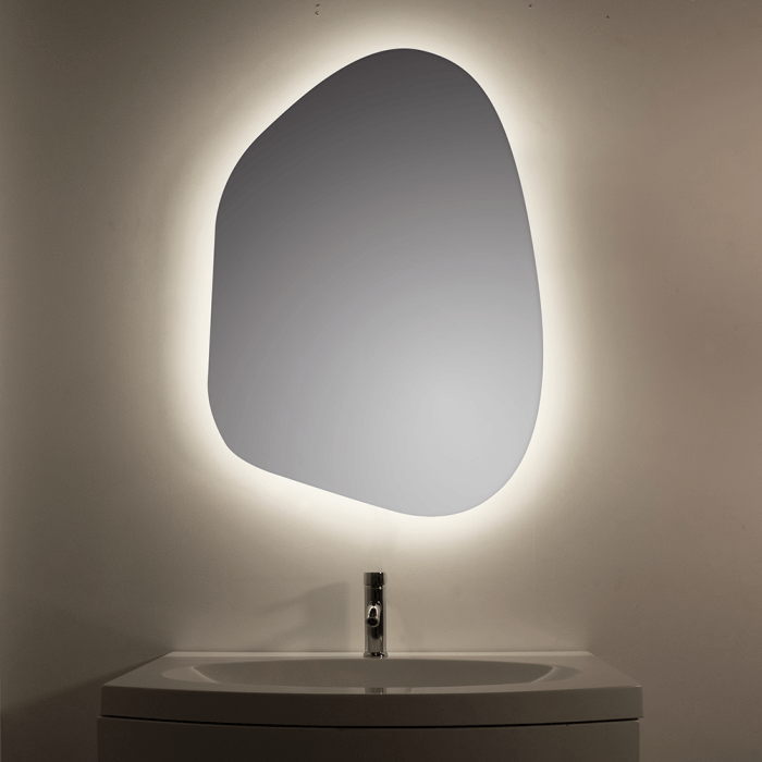 Organic-shaped mirror with backlit illumination above a sink and faucet.
