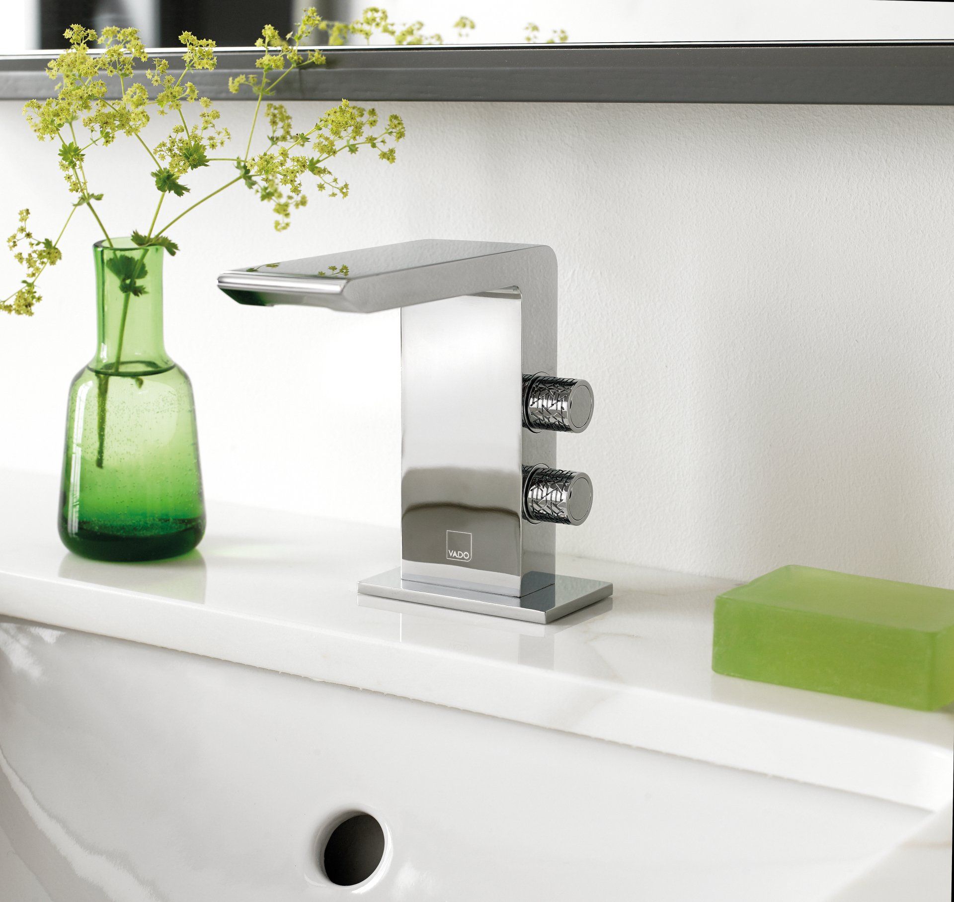 Modern chrome faucet on white countertop, with green vase and soap.