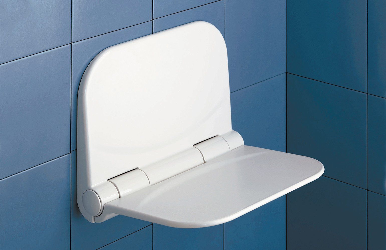 White, wall-mounted, folding shower seat in a bathroom with blue tiles.