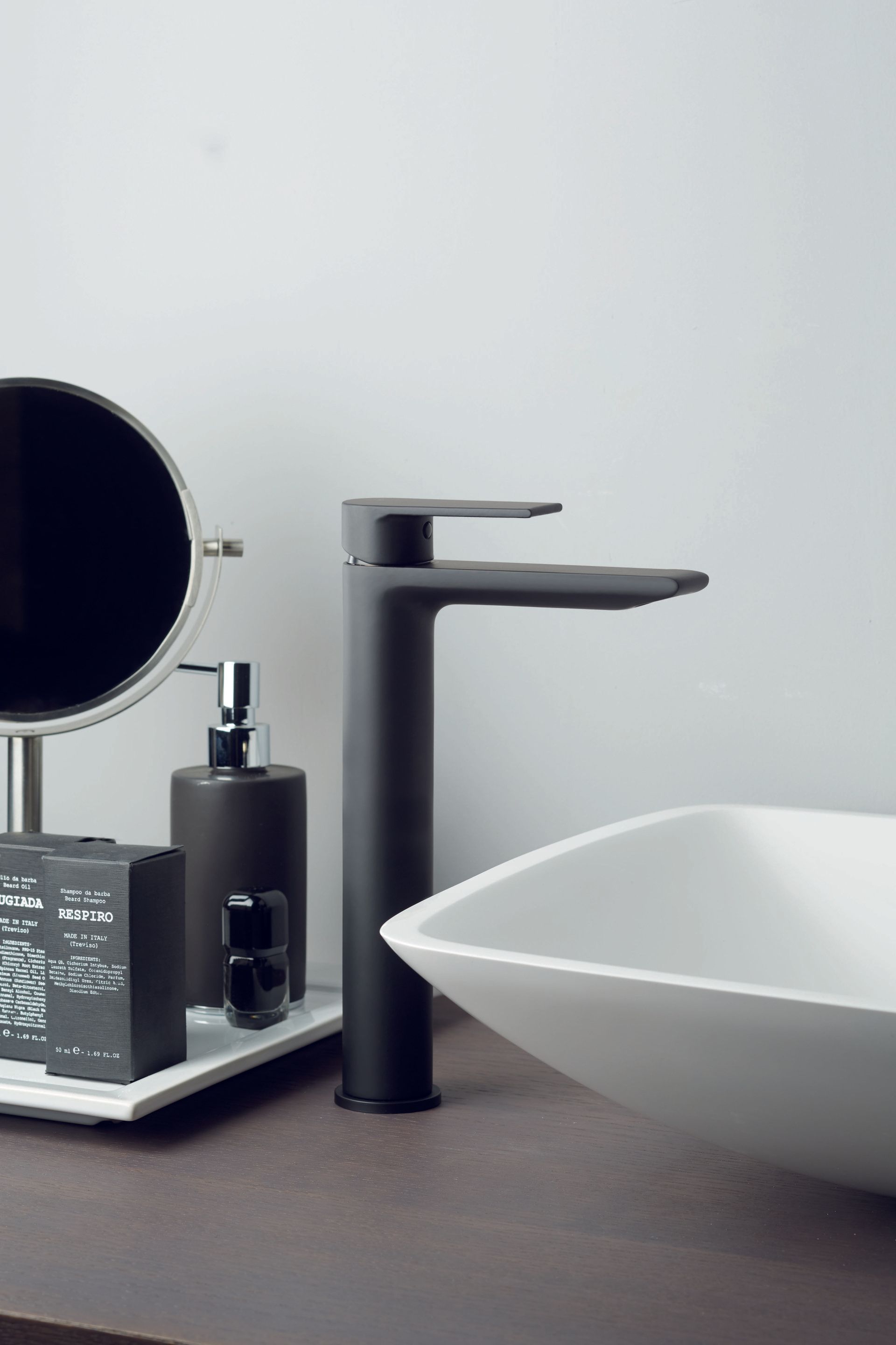 Black faucet, toiletries, and white basin on a dark countertop in a bathroom.