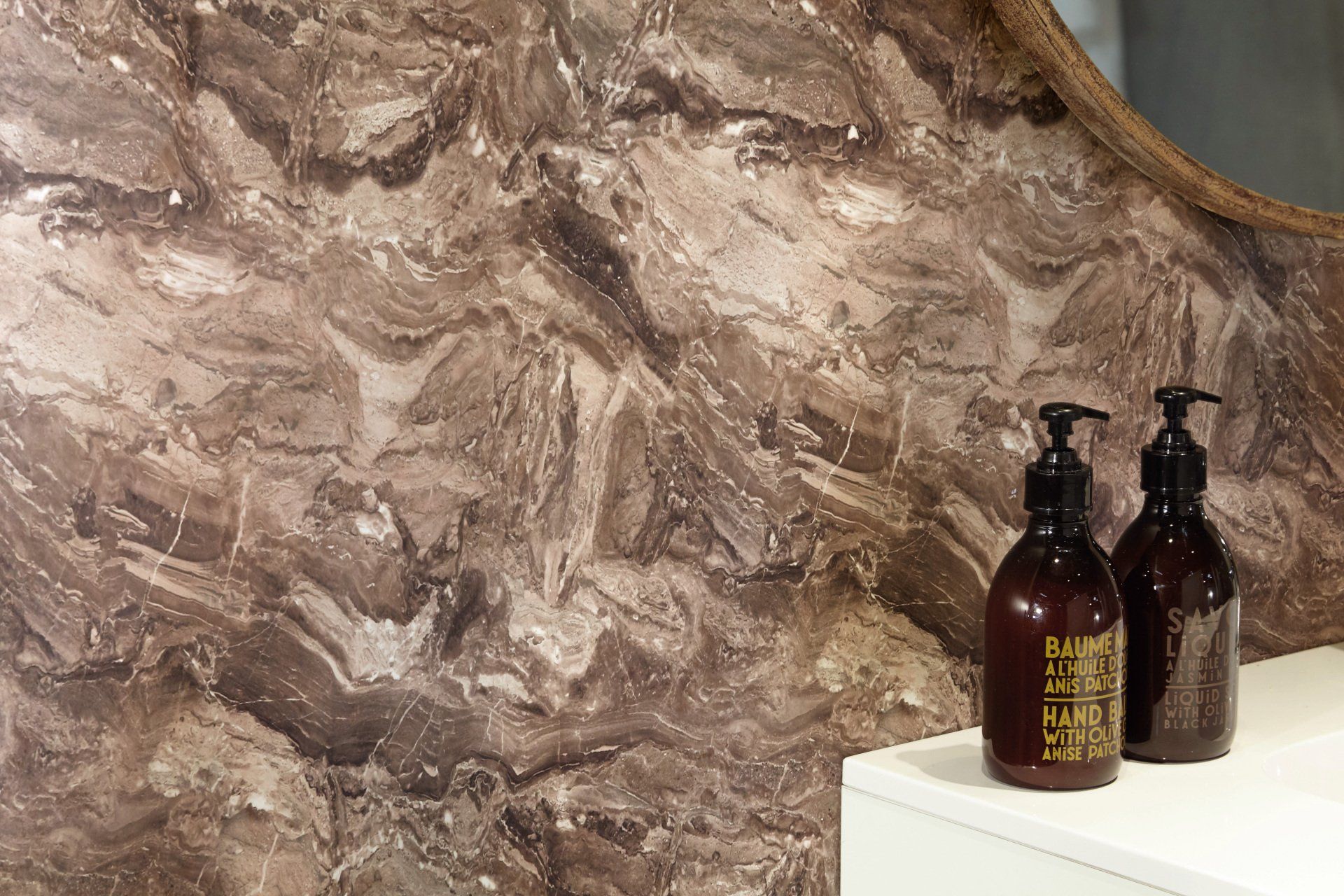 Bathroom with a brown, marble-like wall and two brown soap bottles on a white countertop.
