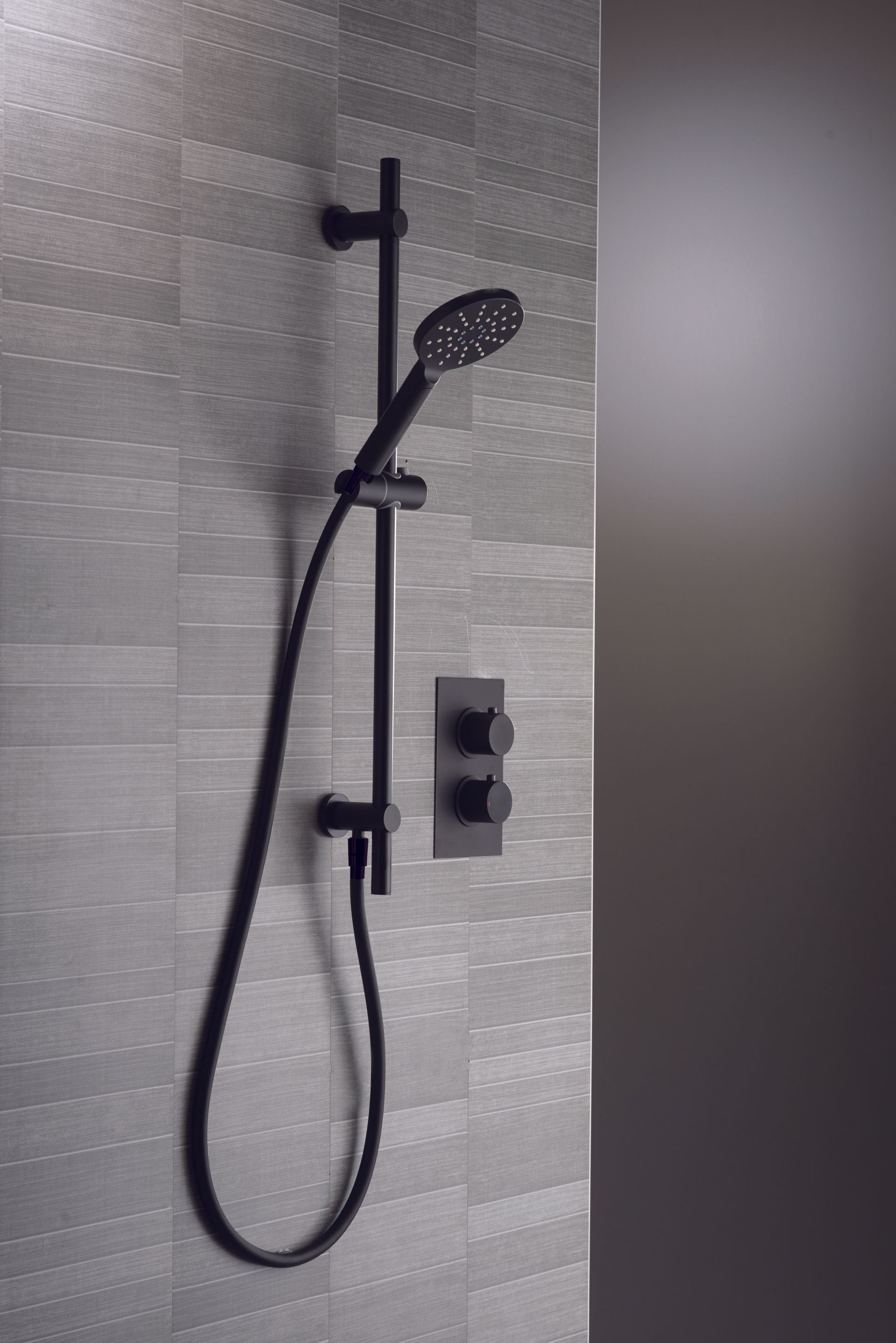 Black shower head and controls on textured gray tiled wall.