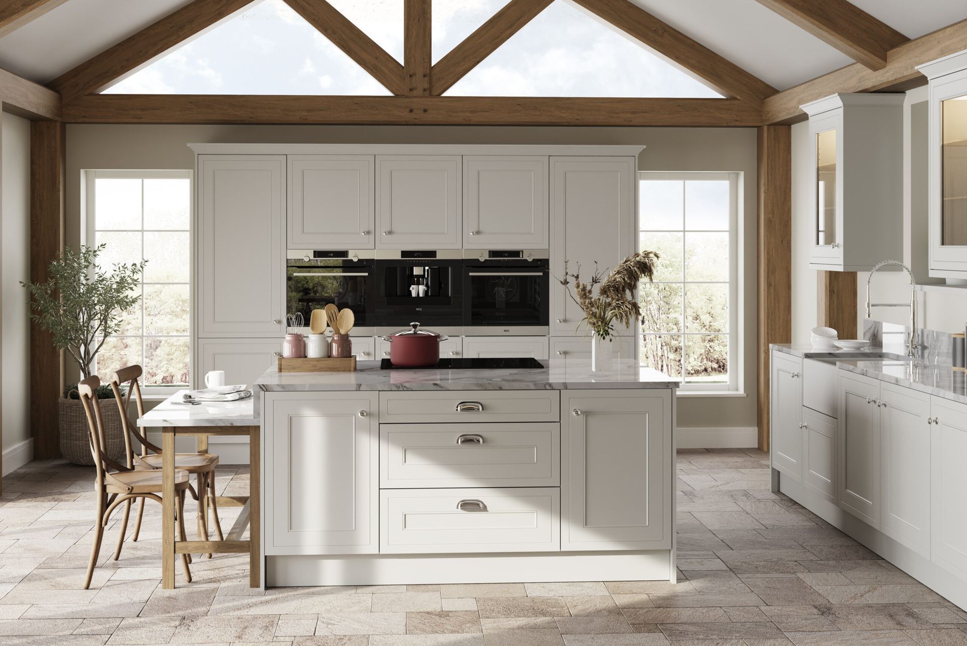 Cream-colored kitchen with island and dining table. Sunlight streams in through windows.