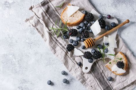 A cutting board topped with bread , blueberries , blackberries , cheese and honey.