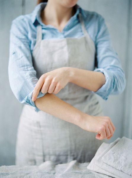 A woman in an apron is scratching her elbow.
