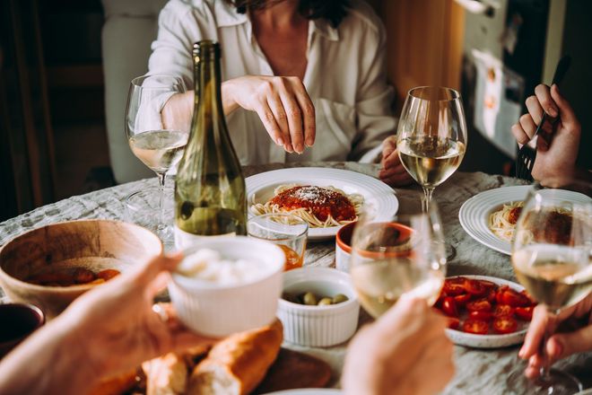 A group of people are sitting at a table eating food and drinking wine.