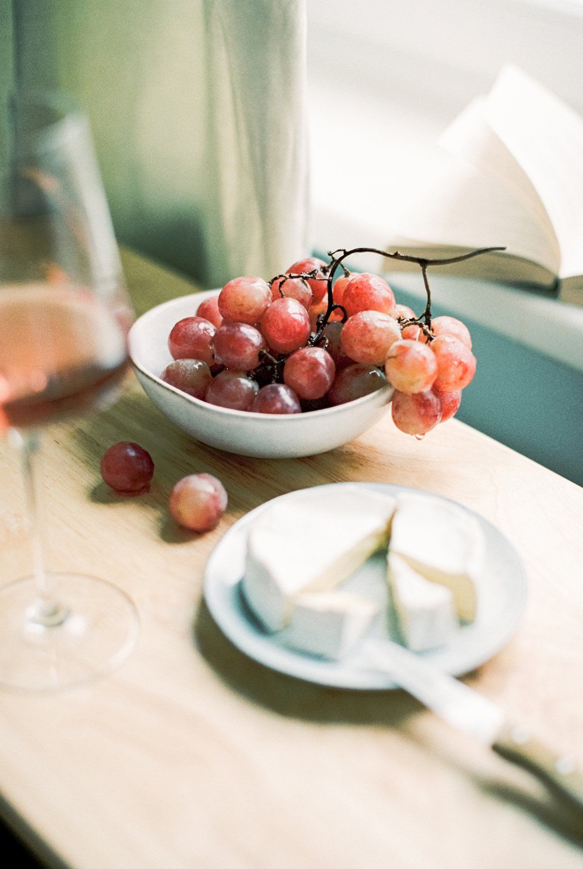 There is a bowl of grapes and a plate of cheese on the table.