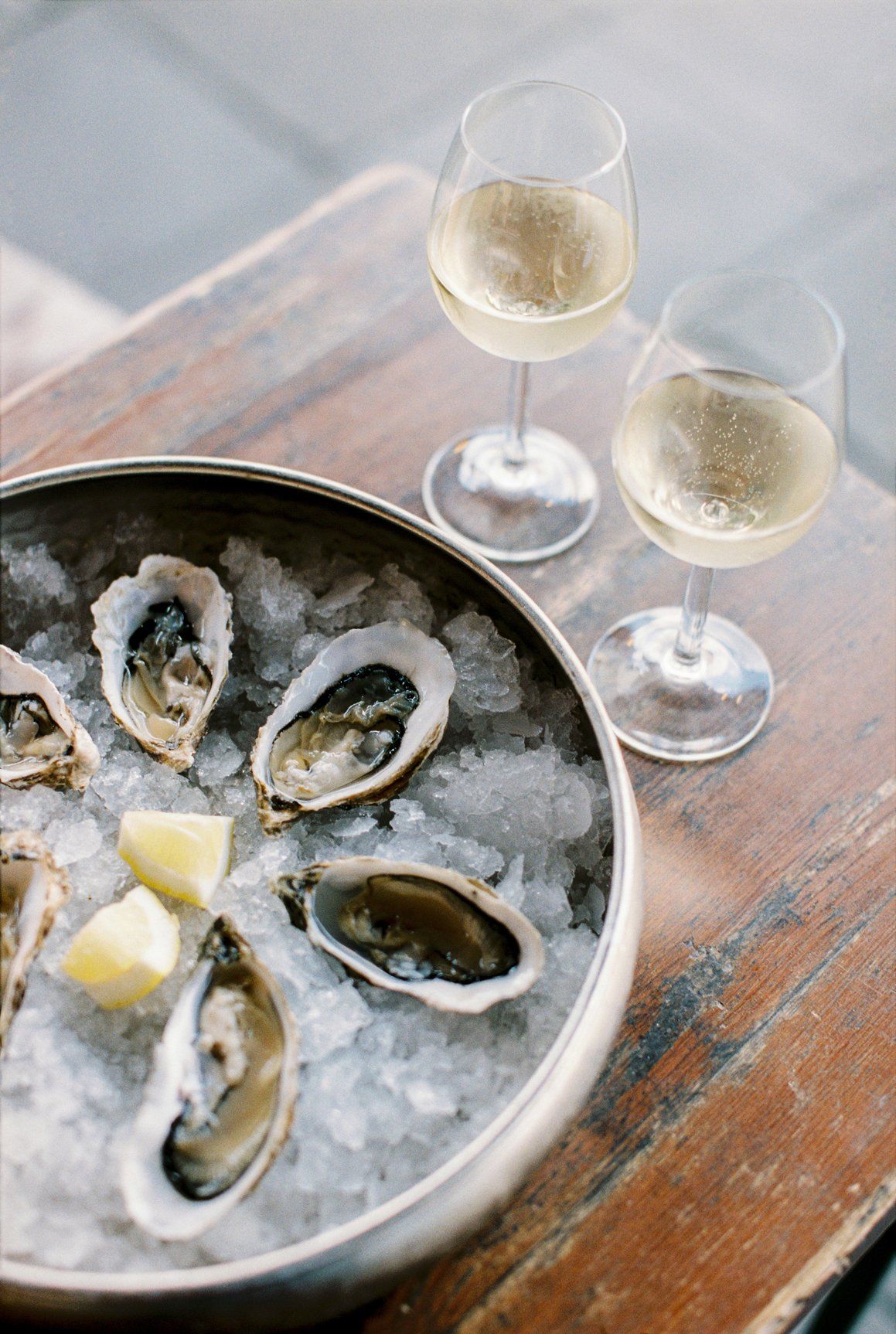 A bowl of oysters on ice next to two glasses of wine.