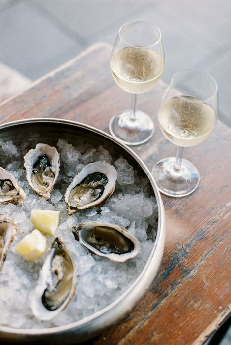 A bowl of oysters on ice next to two glasses of wine.