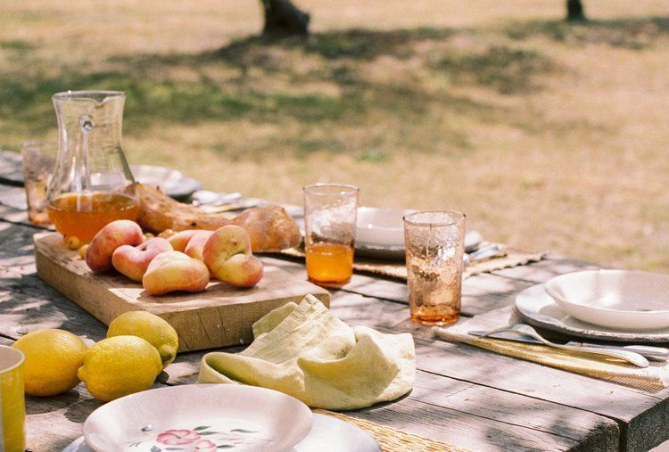 A wooden picnic table with plates, glasses, and fruit for a private catering event.