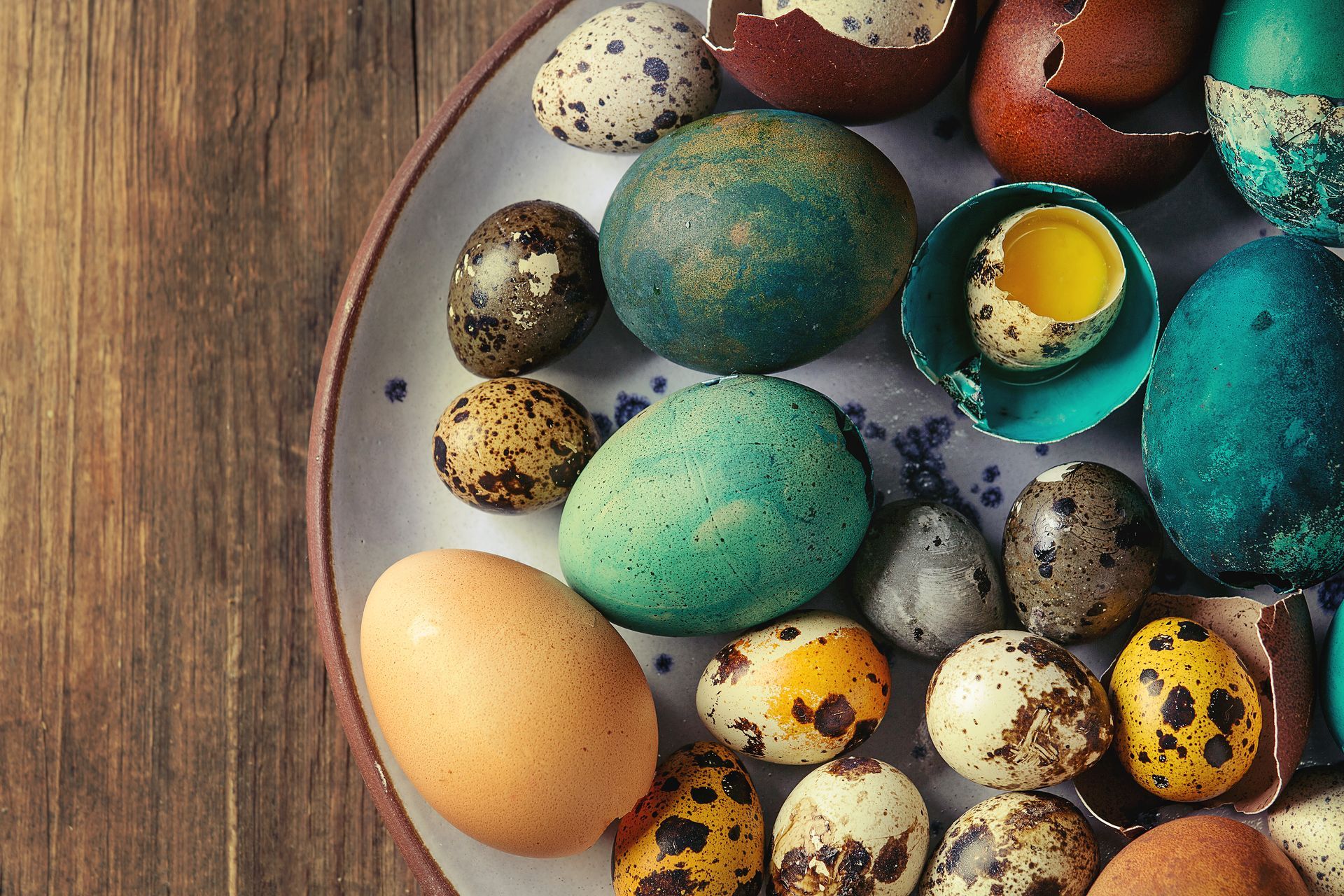 A plate filled with different colored quail eggs on a wooden table.