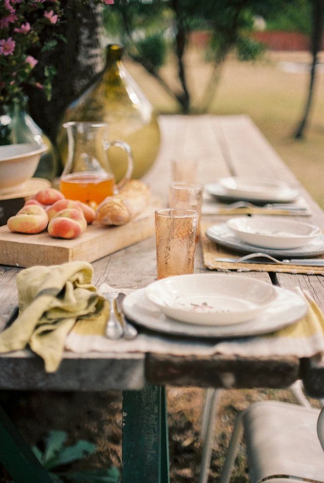 A wooden table with plates , bowls , glasses , and fruit on it.