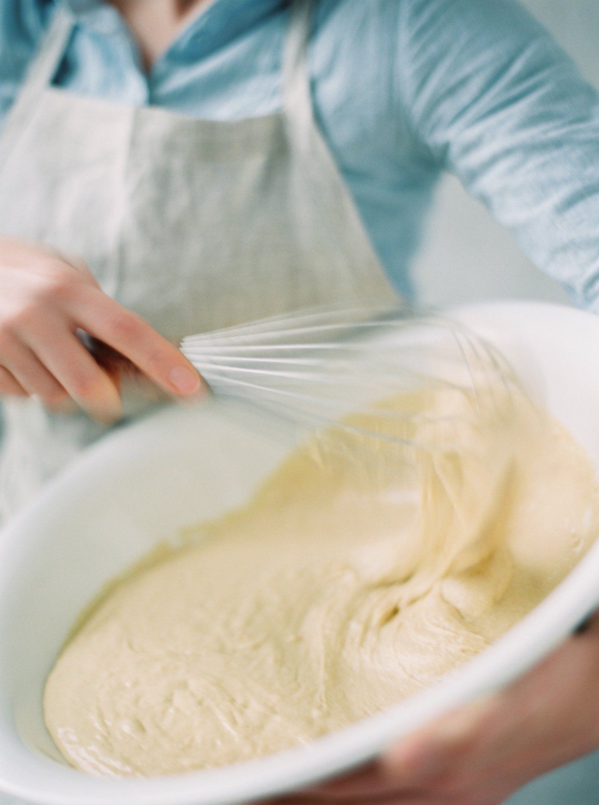 A woman is mixing a batter in a bowl with a whisk.