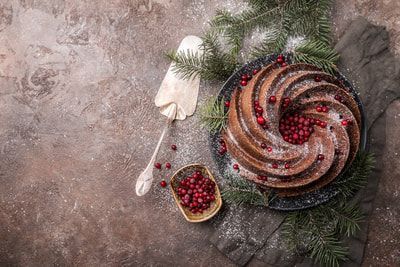 A bundt cake with cranberries and powdered sugar on a plate.