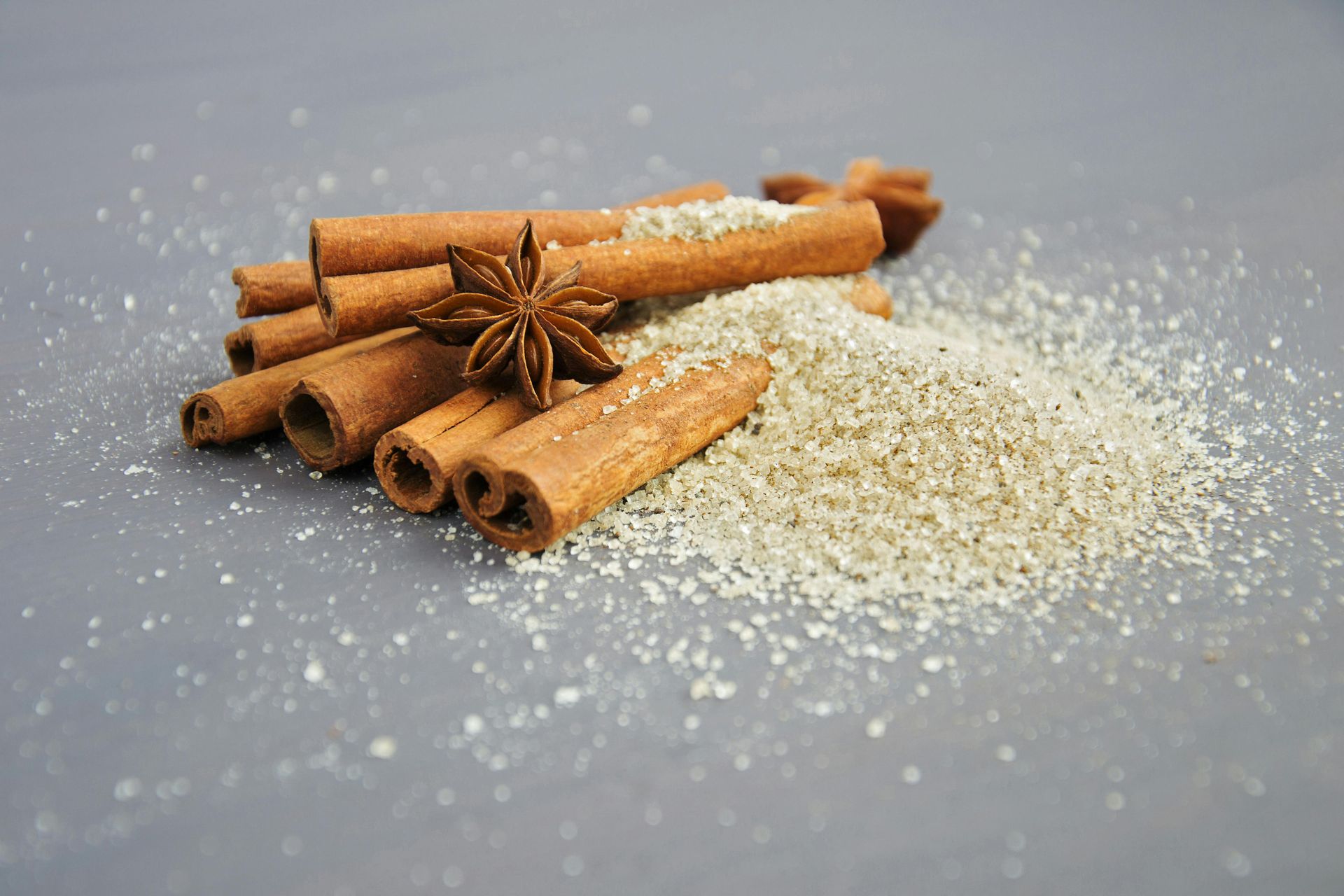 A pile of cinnamon sticks and star anise next to a pile of sugar.