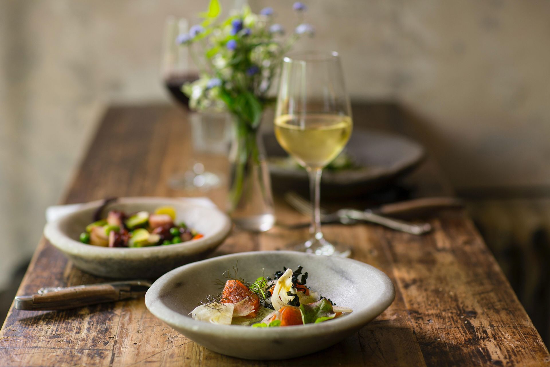 A wooden table topped with two bowls of food and a glass of wine.