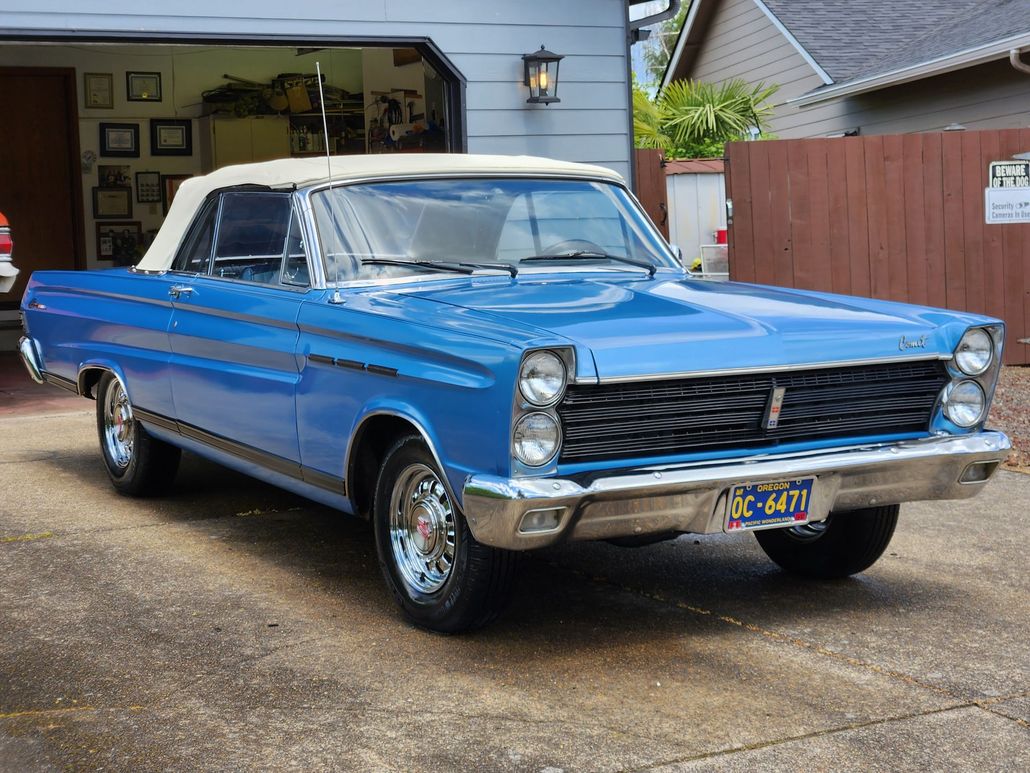 A blue car with a white top is parked in front of a garage.
