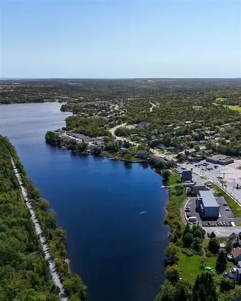 Aerial view of a deep blue river bordered by trees and buildings under a clear sky.