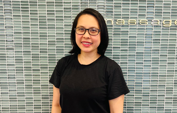 A woman in a black shirt is standing in front of a tiled wall.