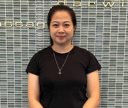 A woman in a black shirt is standing in front of a tiled wall.