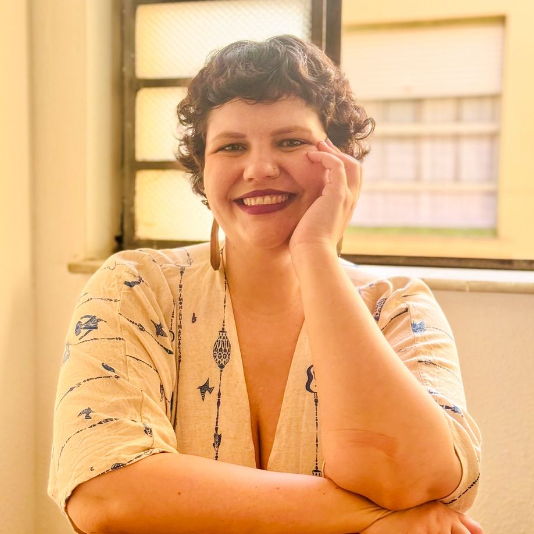 Uma mulher está sorrindo com a mão no rosto em frente a uma janela